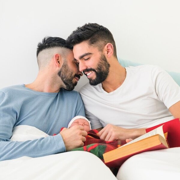 romantic-young-gay-couple-sitting-on-bed-with-their-baby_23-2148083172.jpg